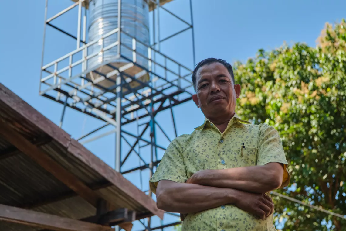 Joy Soth, Chief of the water management committee in Samotr Leu village, knows that the new solar-powered water system (pictured behind) can supply safe, clean water year-round
