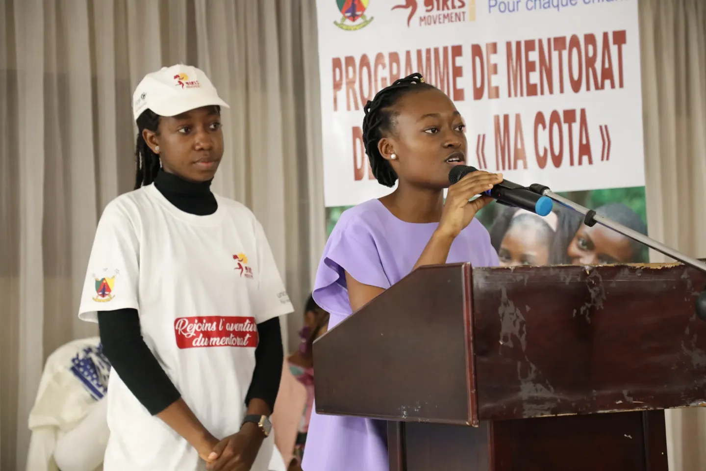 Teen speaking at podium with microphone beside another participant, MA COTA banner behind