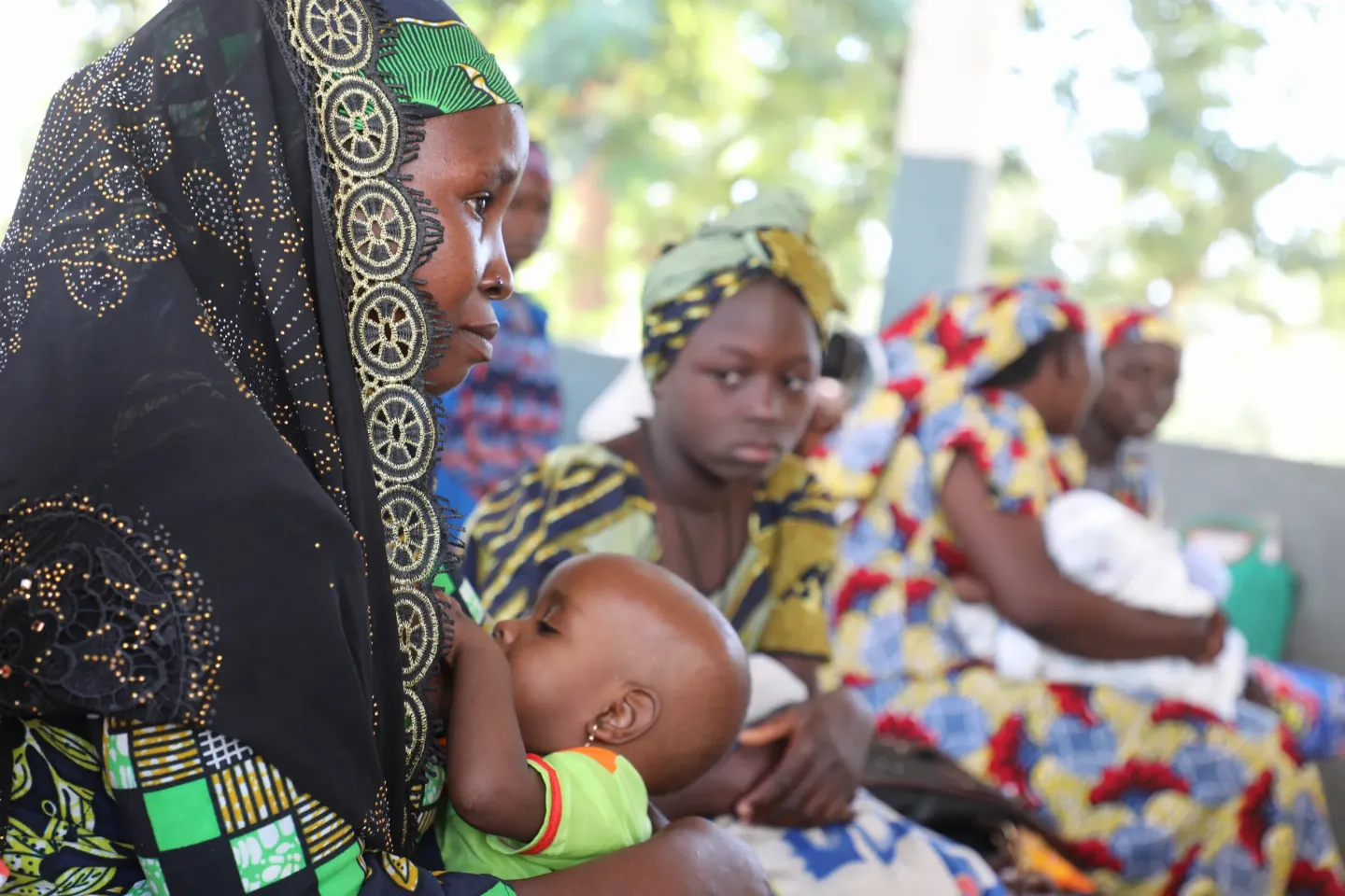 Mother breastfeeding her baby while seated among other women at a health center