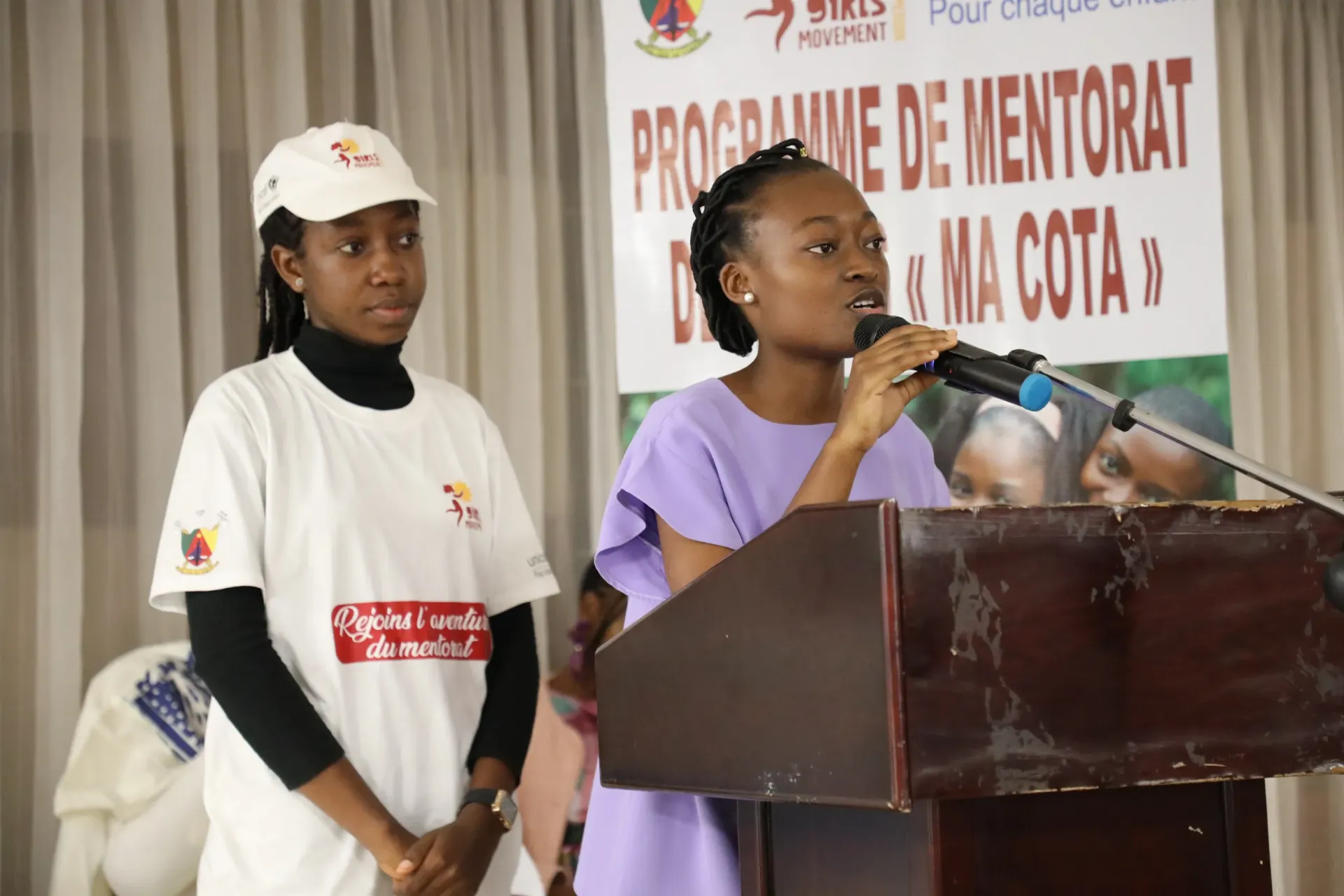 Teen speaking at podium with microphone beside another participant, MA COTA banner behind