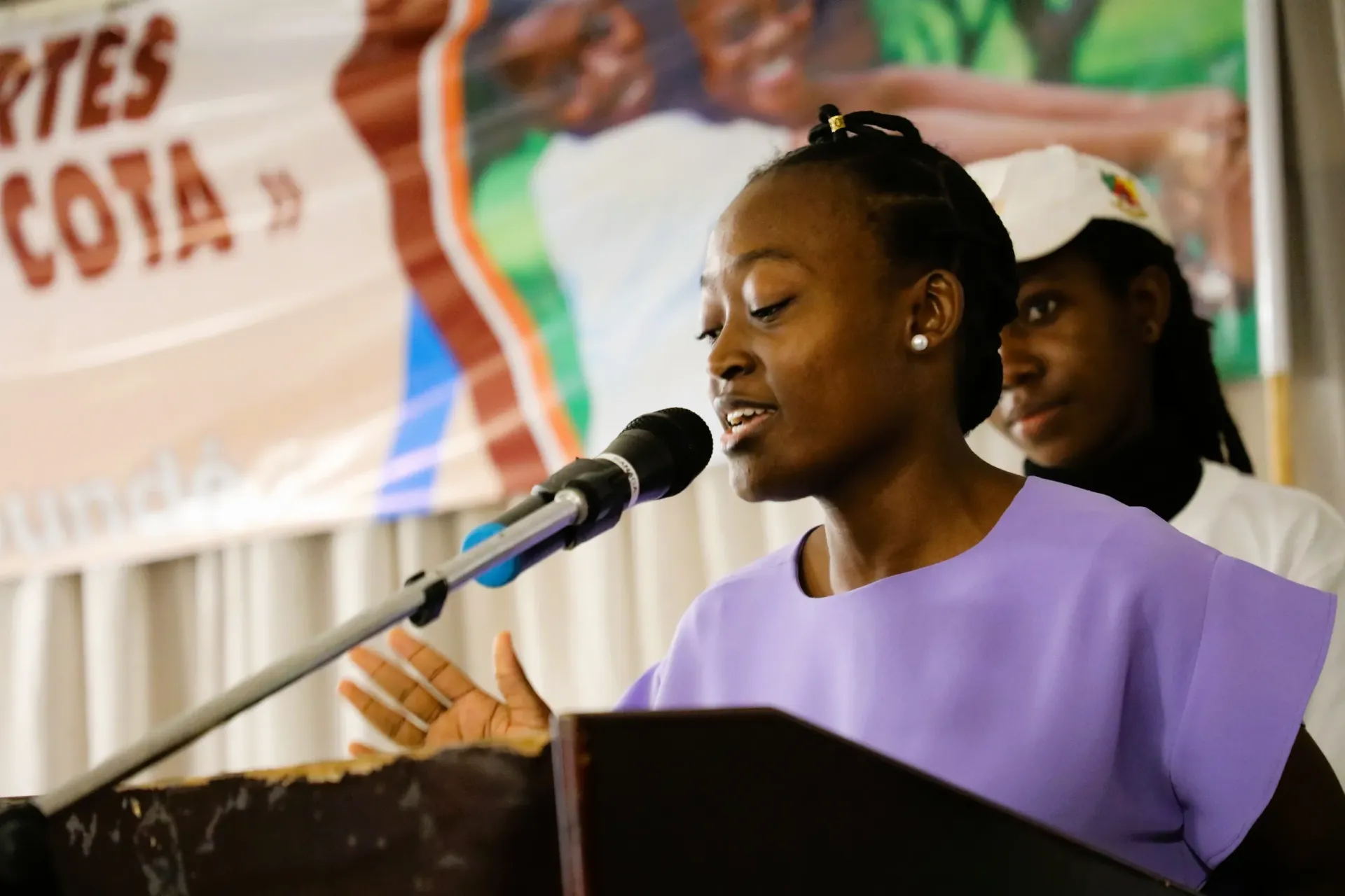 Participant speaking at a podium with microphone during MA COTA mentorship event in Yaound&eacute;