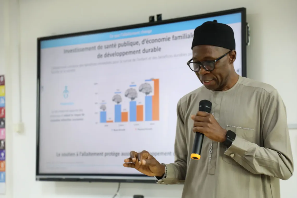 Elhadji, Chief of Nutrition at UNICEF Cameroon, presents key information on the benefits of breastfeeding during a Media Caf&eacute;. A screen displaying data and messages on child health and nutrition is visible in the background.