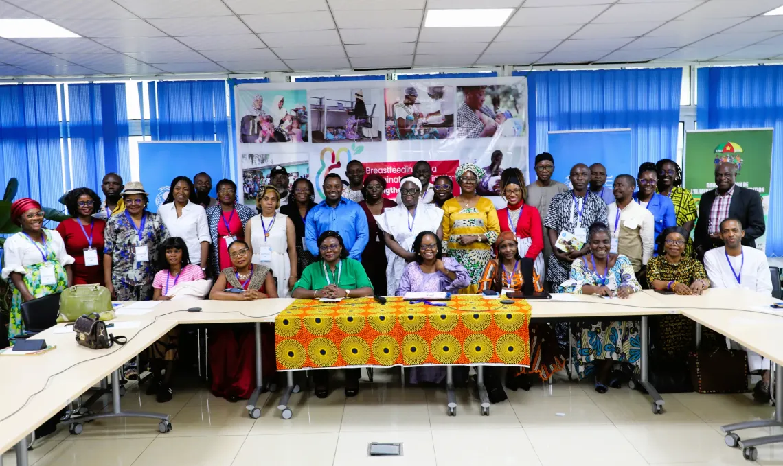 Attendees of the Media Caf&eacute; pose for a group photograph following discussions on breastfeeding and child nutrition. World Breastfeeding Week 2026 campaign banners are visible in the background.