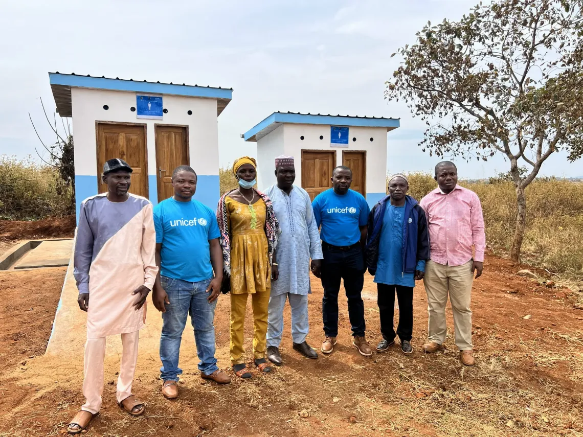 Team gathered before two blue-and-white latrine units at the Bayara health facility