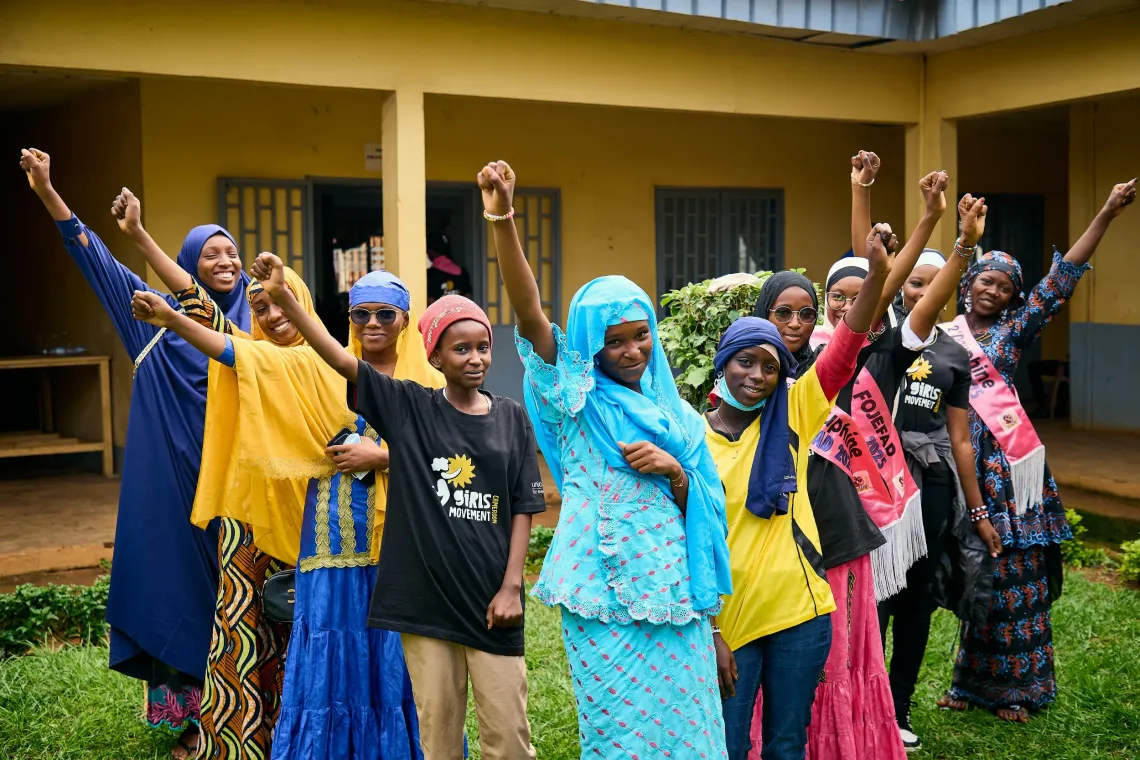 Group of girls raising fists in solidarity during the Girls&rsquo; Movement event, wearing colorful outfits and sashes