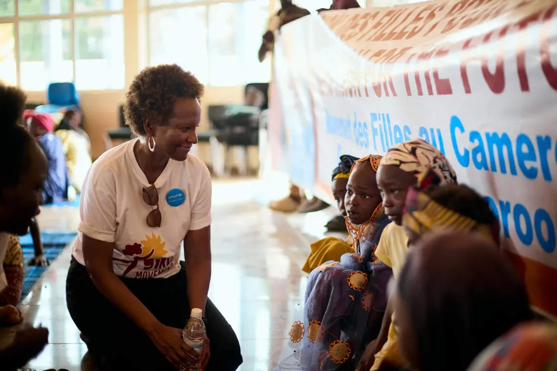 UNICEF Representative in Cameroon kneeling and engaging with participants during the Girls&rsquo; Movement Caravan near a banner promoting girls&rsquo; rights.