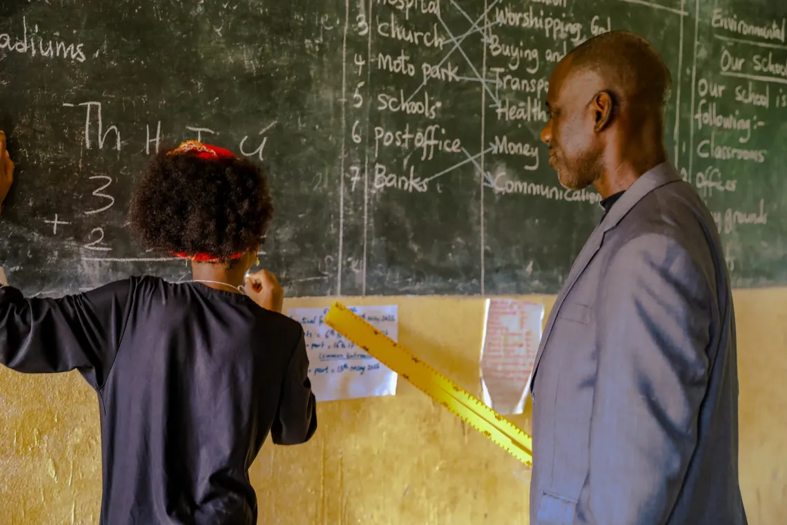 Aminatou is writing on the blackboard near her teacher