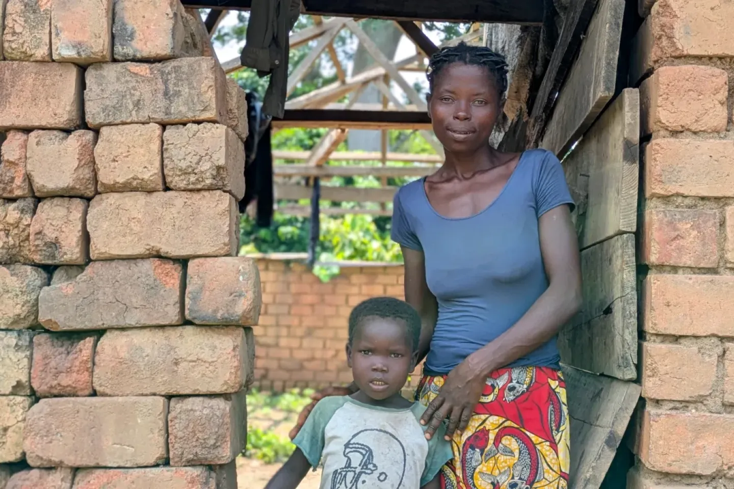 Joseph Ndro, 9, stands with his aunt Fabiola Doubouma in front of their family house in Mondoli village. 