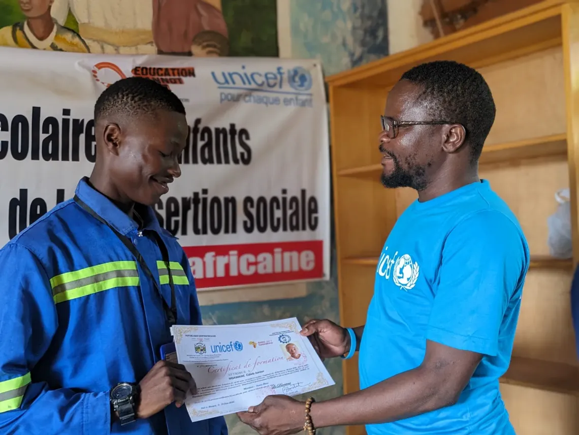 Nestor Yamenedji, from UNICEF, delivers her school certificate to Caleb Junior, the day of the graduation ceremony at Don Bosco Centre