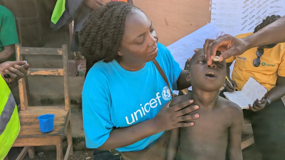 Eve Guiyama, from UNICEF&rsquo;s emergency response team, holds child Alfred while he receives the cholera vaccination drops. 