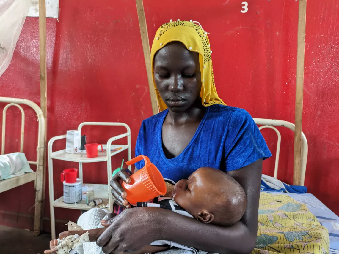 Faida gives a cup of therapeutic milk to her daughter Bintou at the Alindao nutrition centre