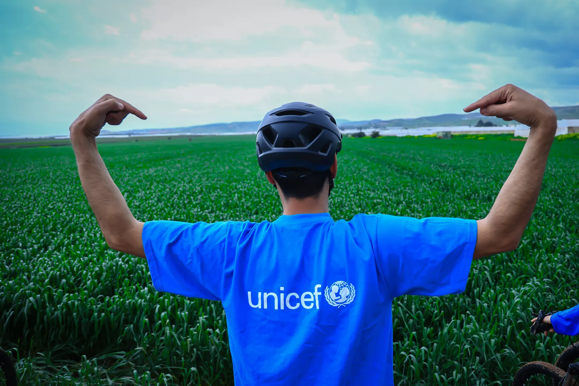 Man wearing a helmet pointing to the back of his cyan blue shirt that reads UNICEF