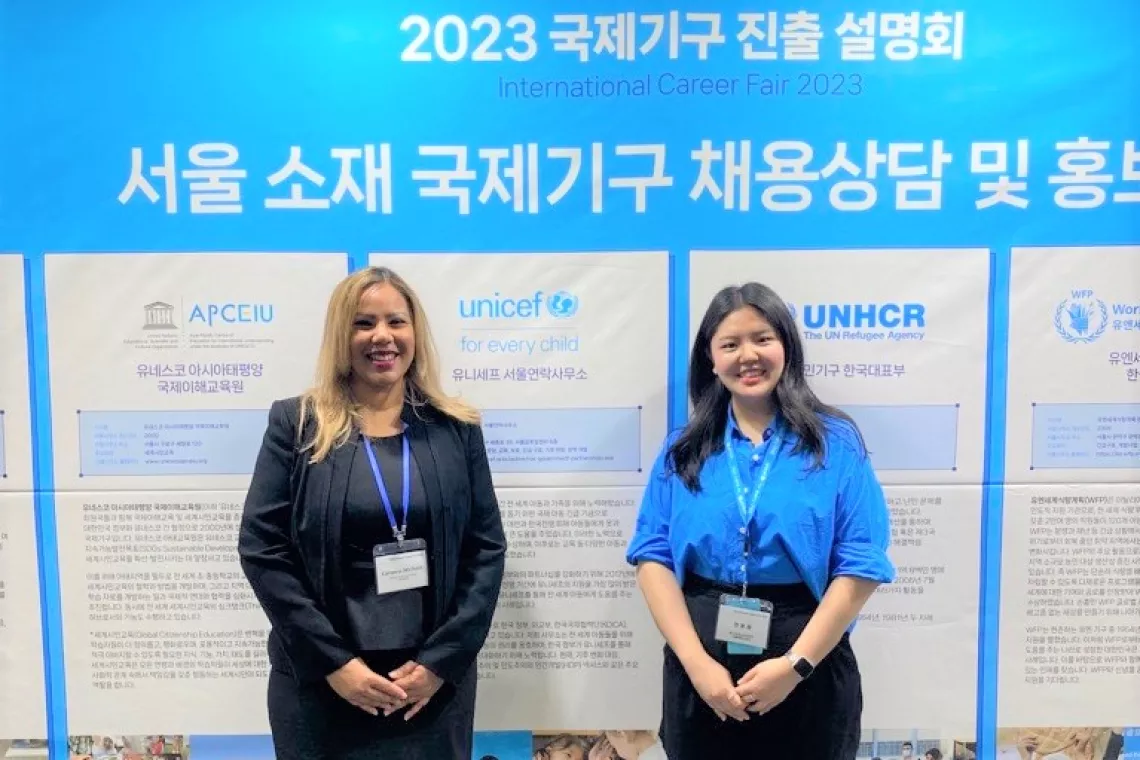 Women standing in front of a board displaying information about UNICEF and UNHCR