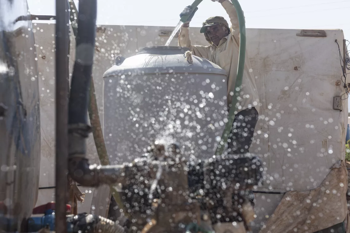 A man opens a tank that provides drinkable water for Syrian refugees in Lebanon