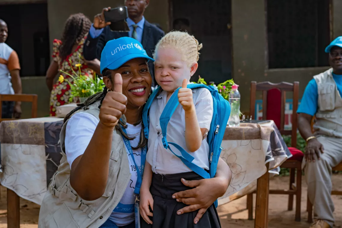 Woman holding a little girl. They both give a thumbs-up to the camera and smile.