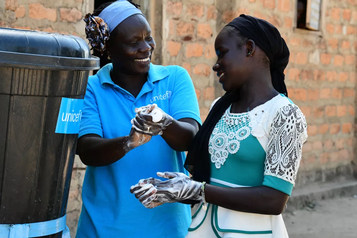 A UNICEF staff, in a hand-washing demonstration to a girl pupil  