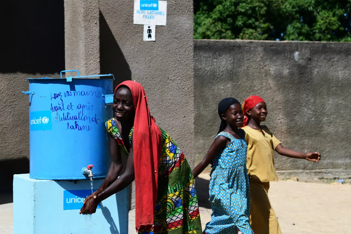 A UNICEF staff, in a hand-washing demonstration to a girl pupil.