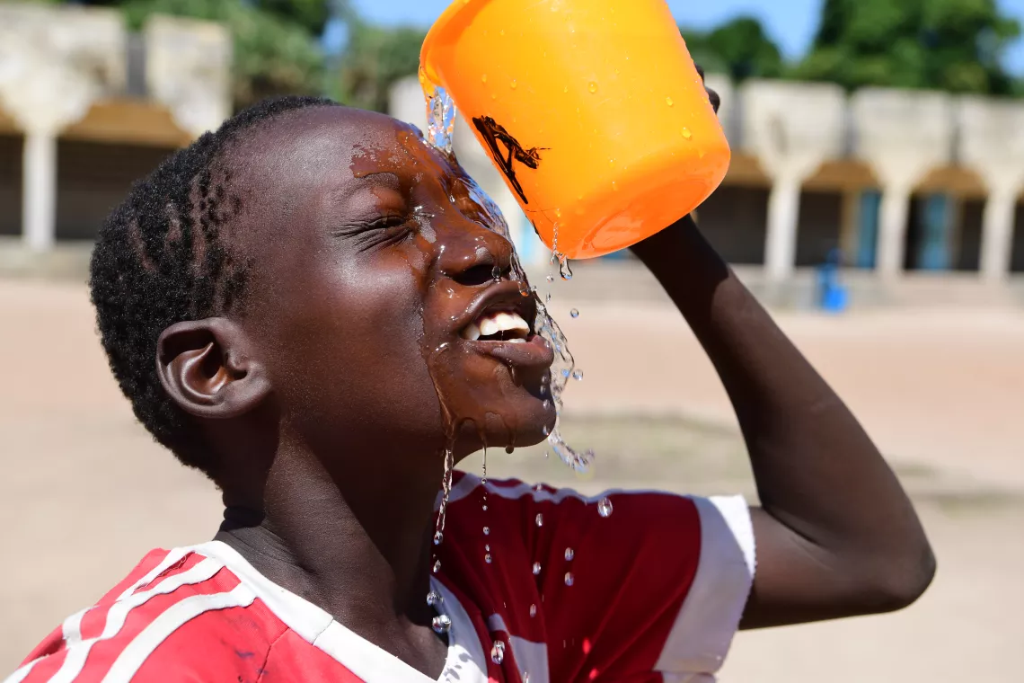An adolescent boy, washing his face in the playground of the school.
