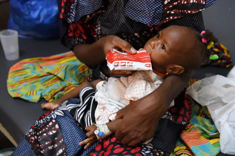 Una madre sostiene en brazos a su hija de 12 meses mientras le da alimento terap&eacute;utico en Burkina Faso
