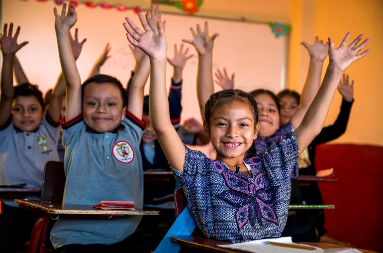 Niños y niñas sonríen mientras están sentados en sus escritorios en una escuela rural de Guatemala