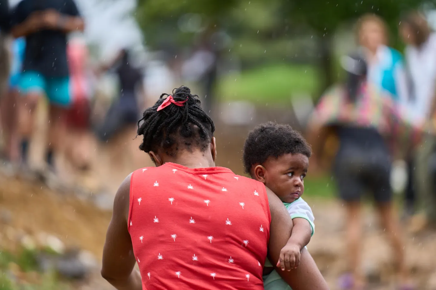 A woman carrying a child with raindrops starting to fall.