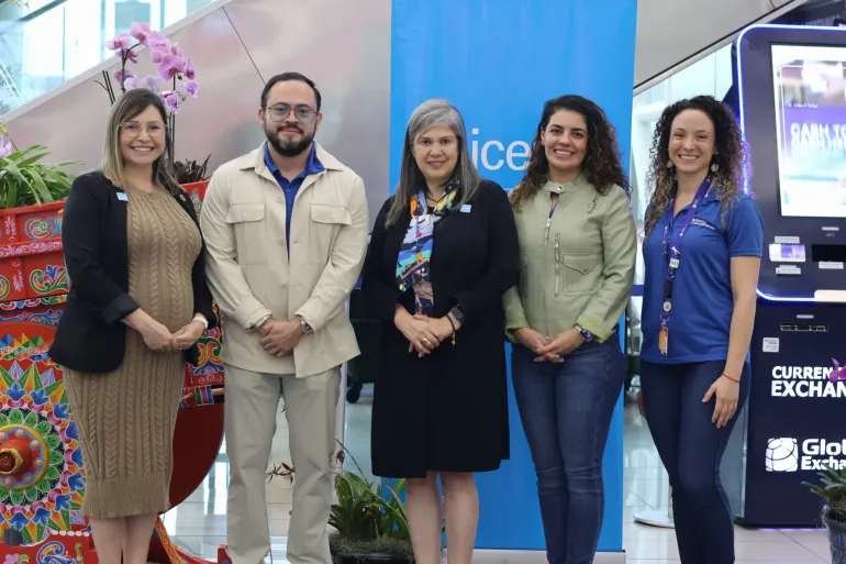 El equipo de UNICEF y de AERIS miran a la c&aacute;mara frente al banner y una carreta t&iacute;pica en el aeropuerto Juan Santamar&iacute;a.