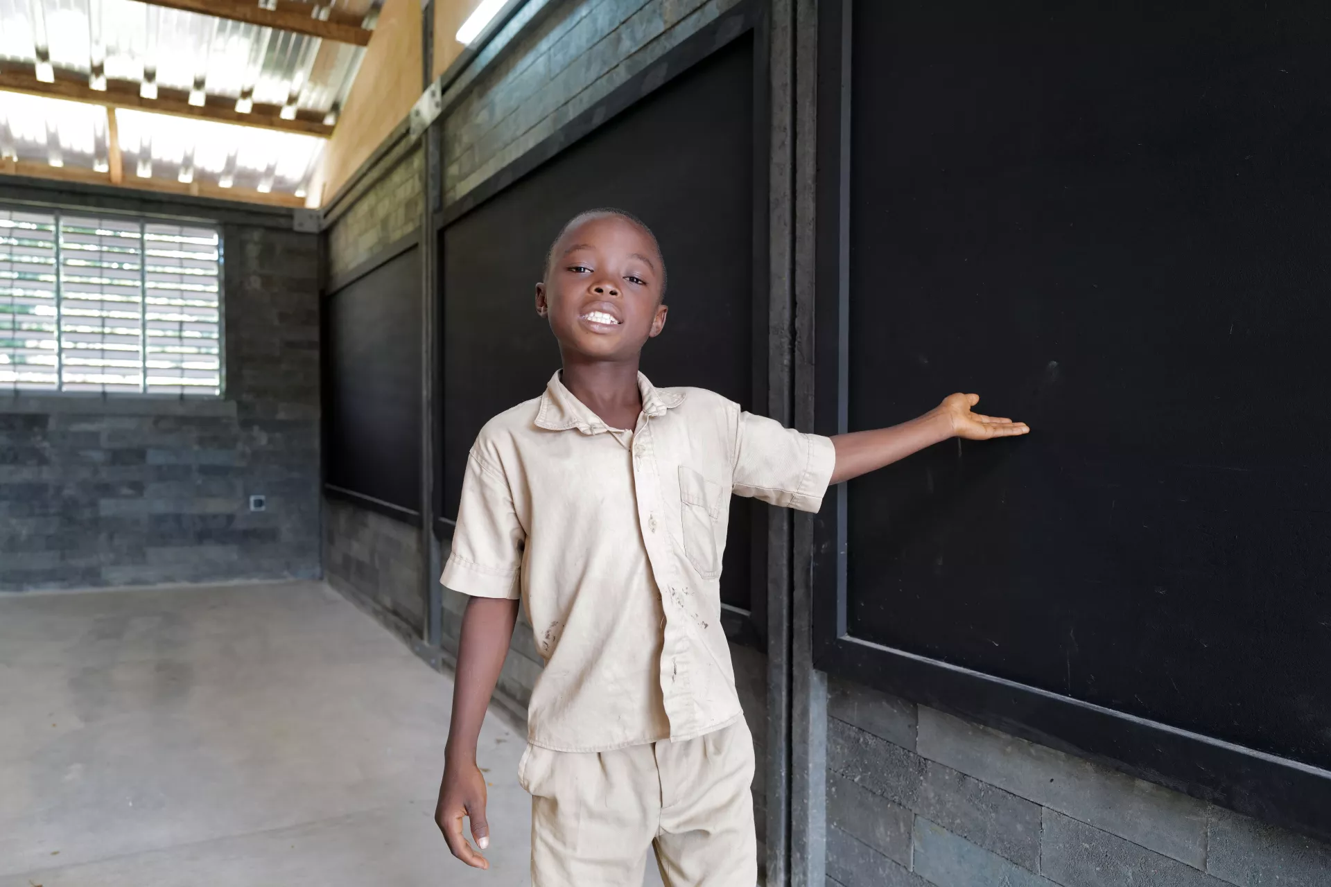 Ange Emmanuel montre fi&egrave;rement sa nouvelle classe faite en briques de plastique