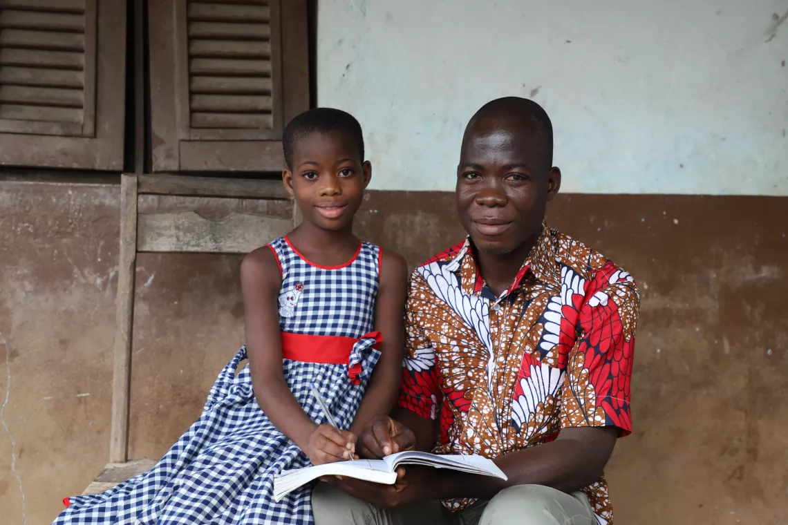 Ars&egrave;ne Tind&eacute;, a 39-year-old teacher, helps his 8 year old daughter Anne with her homework on the porch of their house in Toumoudi-Sakassou in C&ocirc;te d&rsquo;Ivoire.
