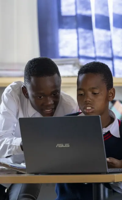 Ntombifuthi Mahlangu (R) an Expanded Public works coordinator at Bophelong Empilweni Community Project assists learners on a laptop computer with their homework on October 1, 2024 in Tembisa township, South Africa.