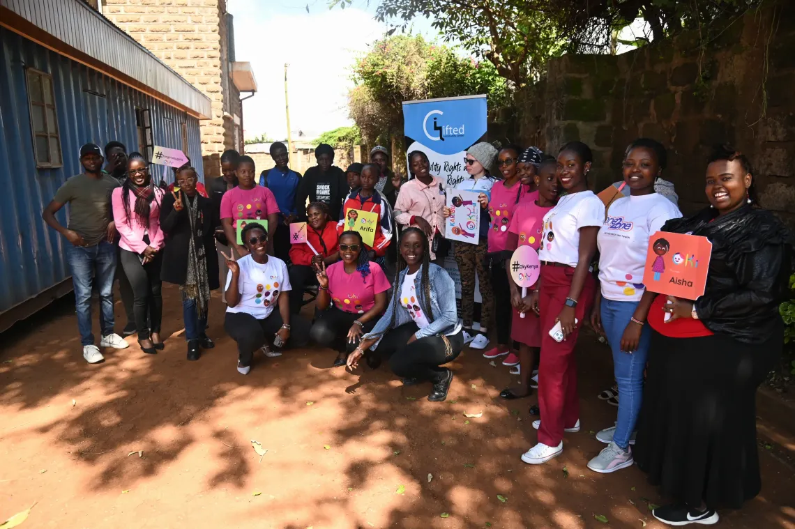 A group of young women with disabilities from Kenya, as well as members of LVCT Health and Gifted Community Centre, are posing for the picture and holding Oky signs.