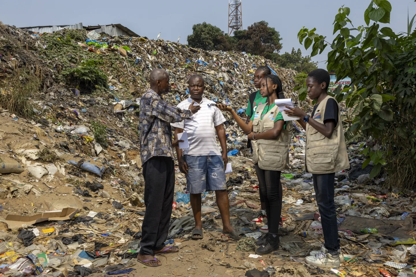Un groupe d'enfant et d'adultes devant un amas de d&eacute;chets.