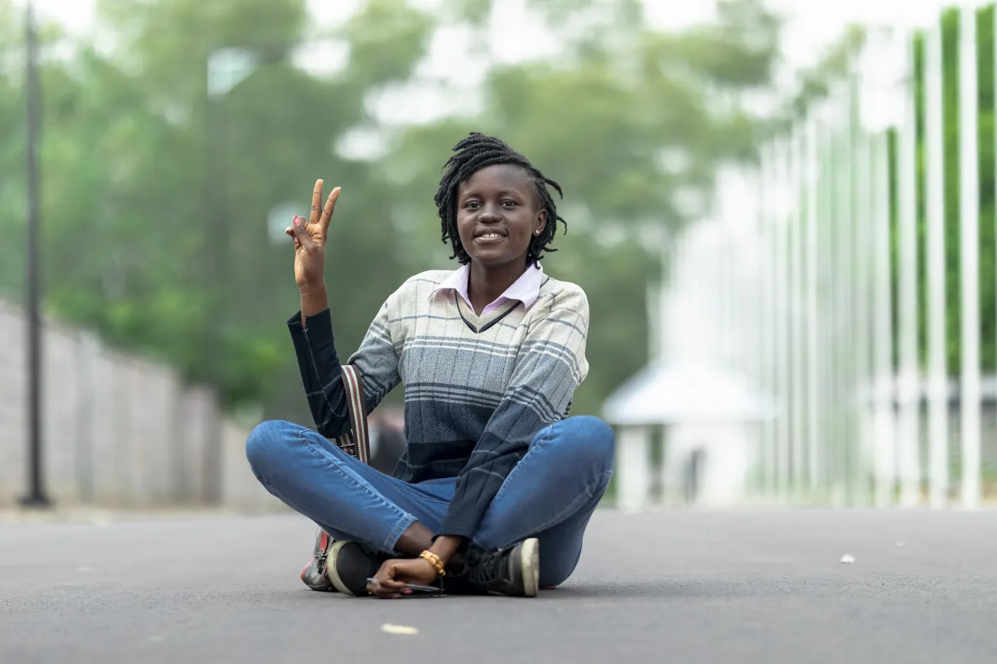 Une jeune femme assise par terre, l&egrave;ve la main et fait un signe V avec les doigts