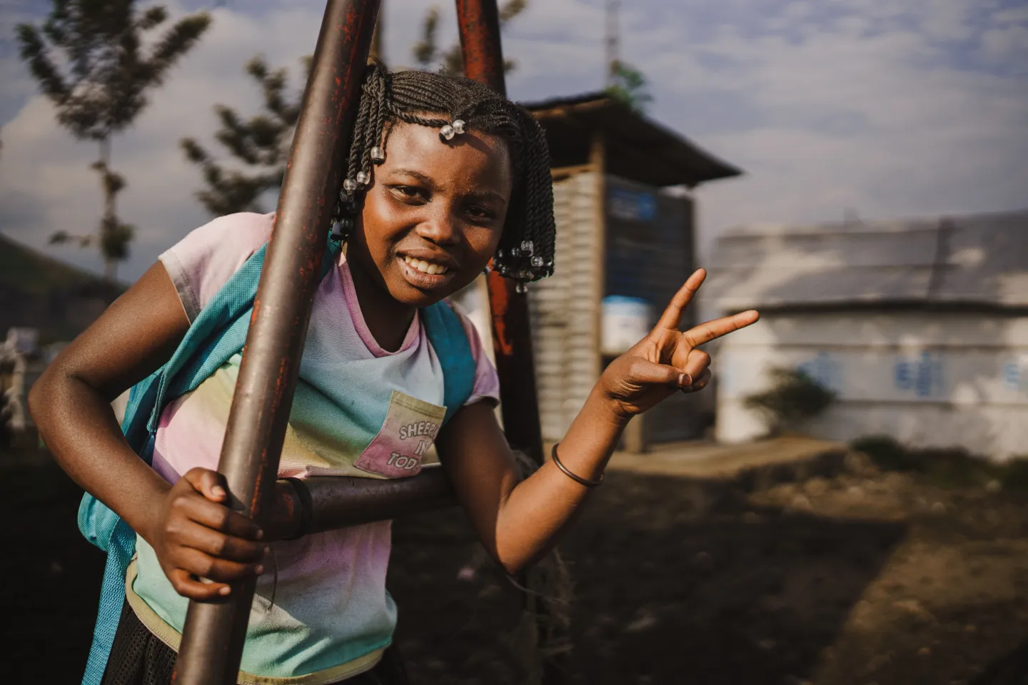 Une fille se tient &agrave; la structure d'une balan&ccedil;oire en souriant et en faisant un signe V avec sa main