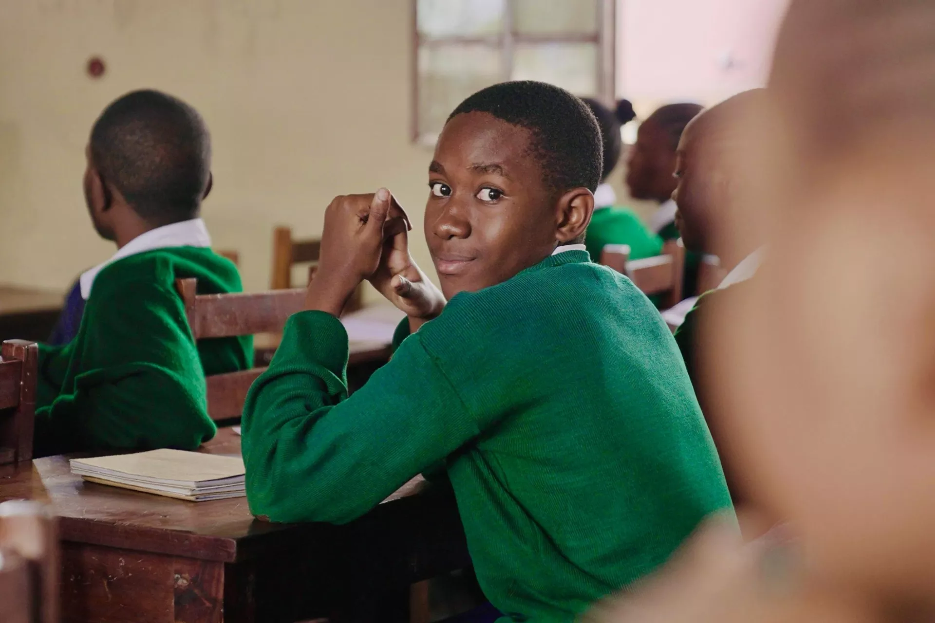 A boy in school uniform sitting on a wooden bench