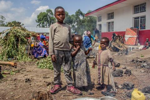 Trois enfants déplacé se tenant au milieu de la cours d'une école primaire où ils ont trouvé refuge