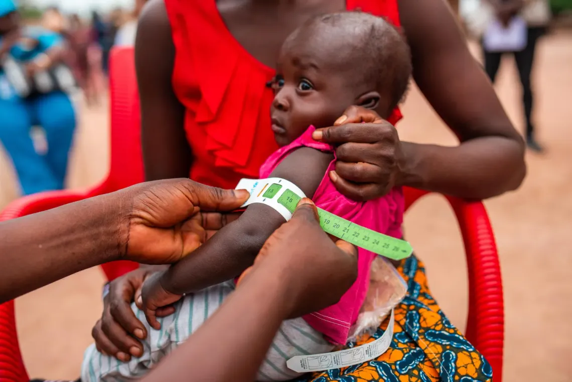 Un enfant se fait mesurer le haut du bras en &eacute;tant assis sur les genoux de sa m&egrave;re