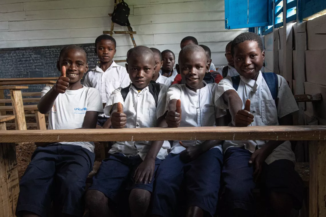 Four children give a thumbs-up as they sit on a wooden bench