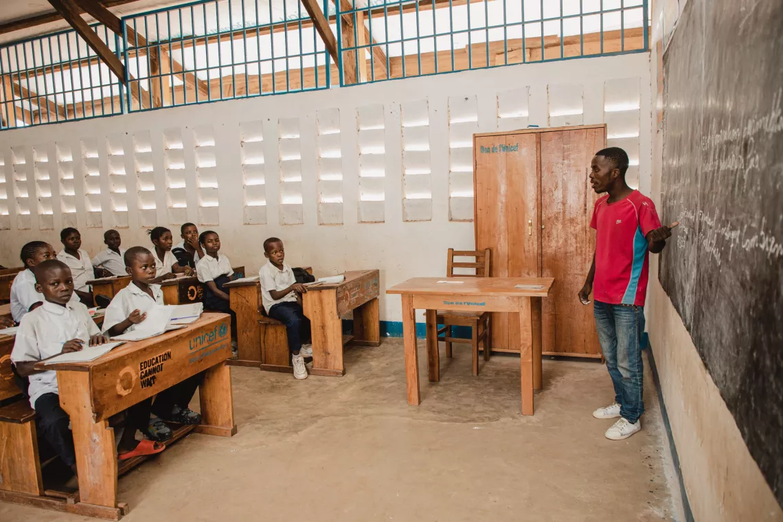 Un enseignent se tient au tableau dans une salle de classe avec des &eacute;l&egrave;ves assis &agrave; leurs bancs