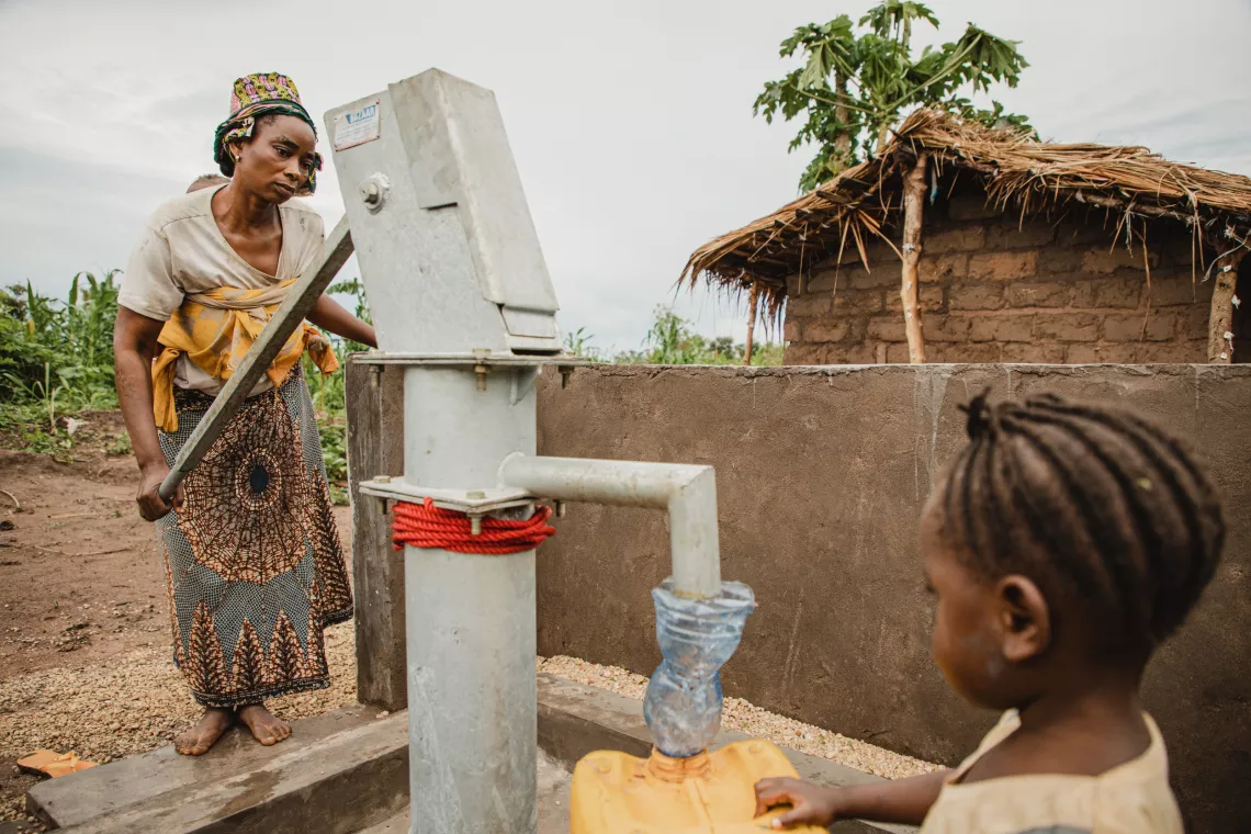Un femme et une fille s'approvisionnent en eau &agrave; une borne fontaine manuelle