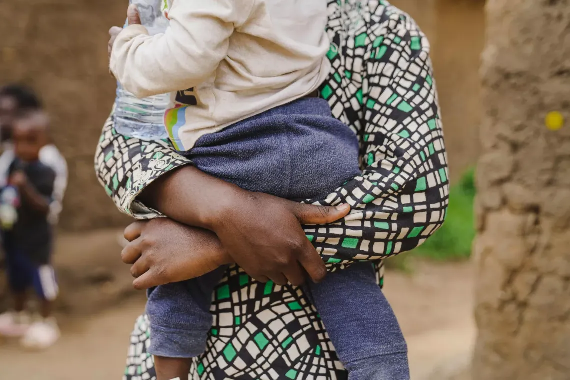 Un enfant, vu de dos, port&eacute; dans les bras par une fille habill&eacute;e d'une chemise color&eacute;e