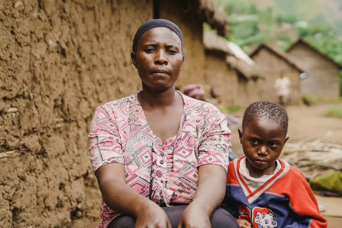 Une femme, assise &agrave; c&ocirc;t&eacute; d'un enfant, devant des maisons en terre