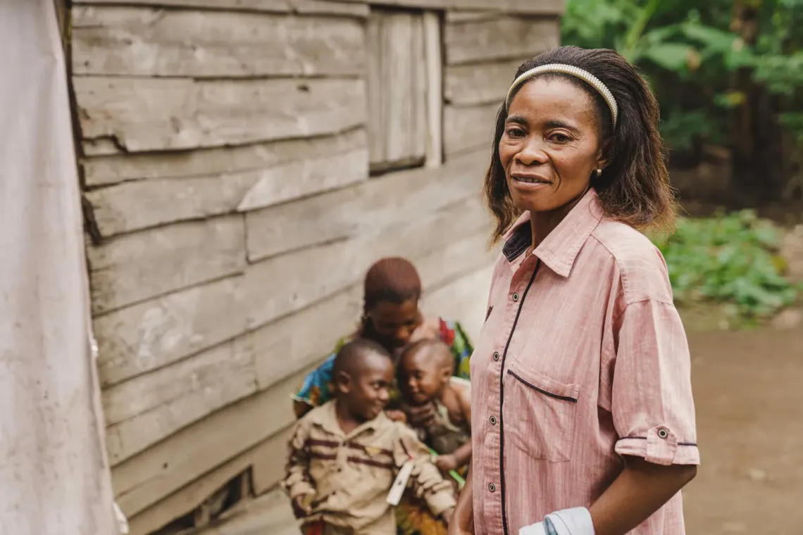Une femme regardant devant elle, avec une seconde femme en arri&egrave;re plan qui porte deux enfants sur ses genoux