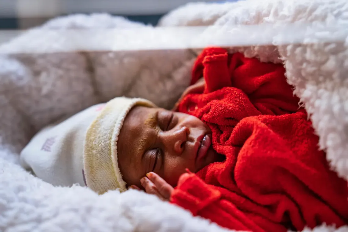 Un nouveau n&eacute; habill&eacute; en rouge, avec un bonnet blanc, dort dans une couveuse