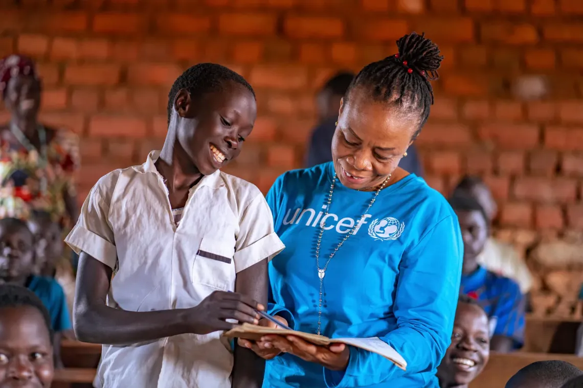 Une coll&egrave;gue de l'UNICEF regarde le cahier d'une el&egrave;ve qui se tient debout &agrave; c&ocirc;t&eacute; d'elle