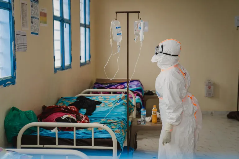 Une professionnelle de sant&eacute; en tenue de protection int&eacute;grale v&eacute;rifie une perfusion dans une salle d'isolement.