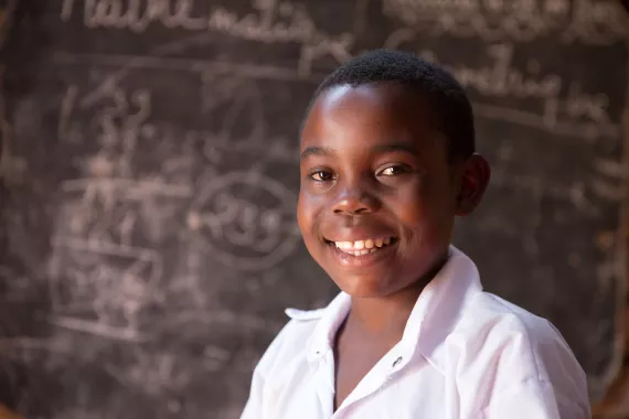 Un &eacute;l&egrave;ve souriant devant le tableau de sa salle de classe
