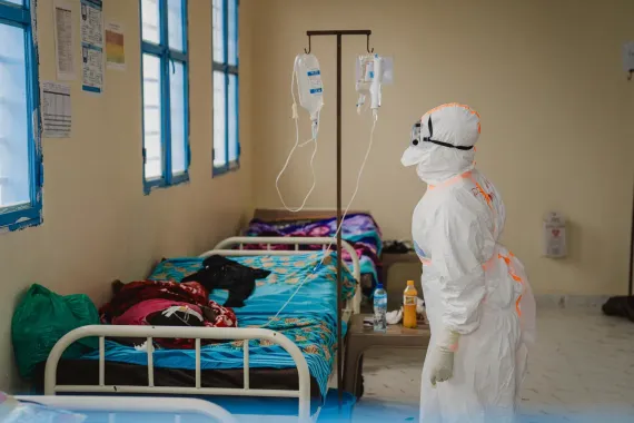 Une professionnelle de santé en tenue de protection intégrale vérifie une perfusion dans une salle d'isolement.