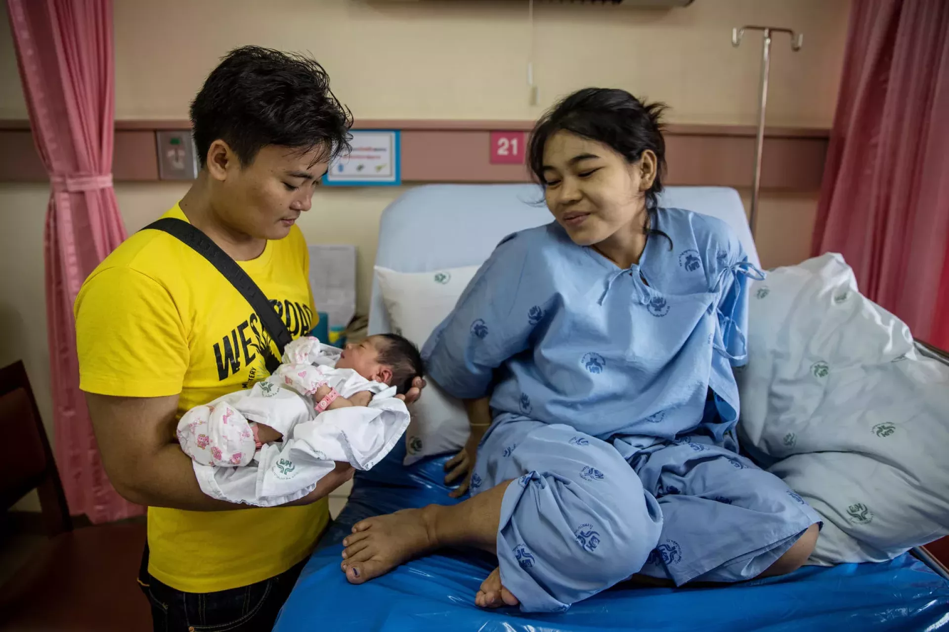 A new father holds his newborn next to the mother on a hospital bed