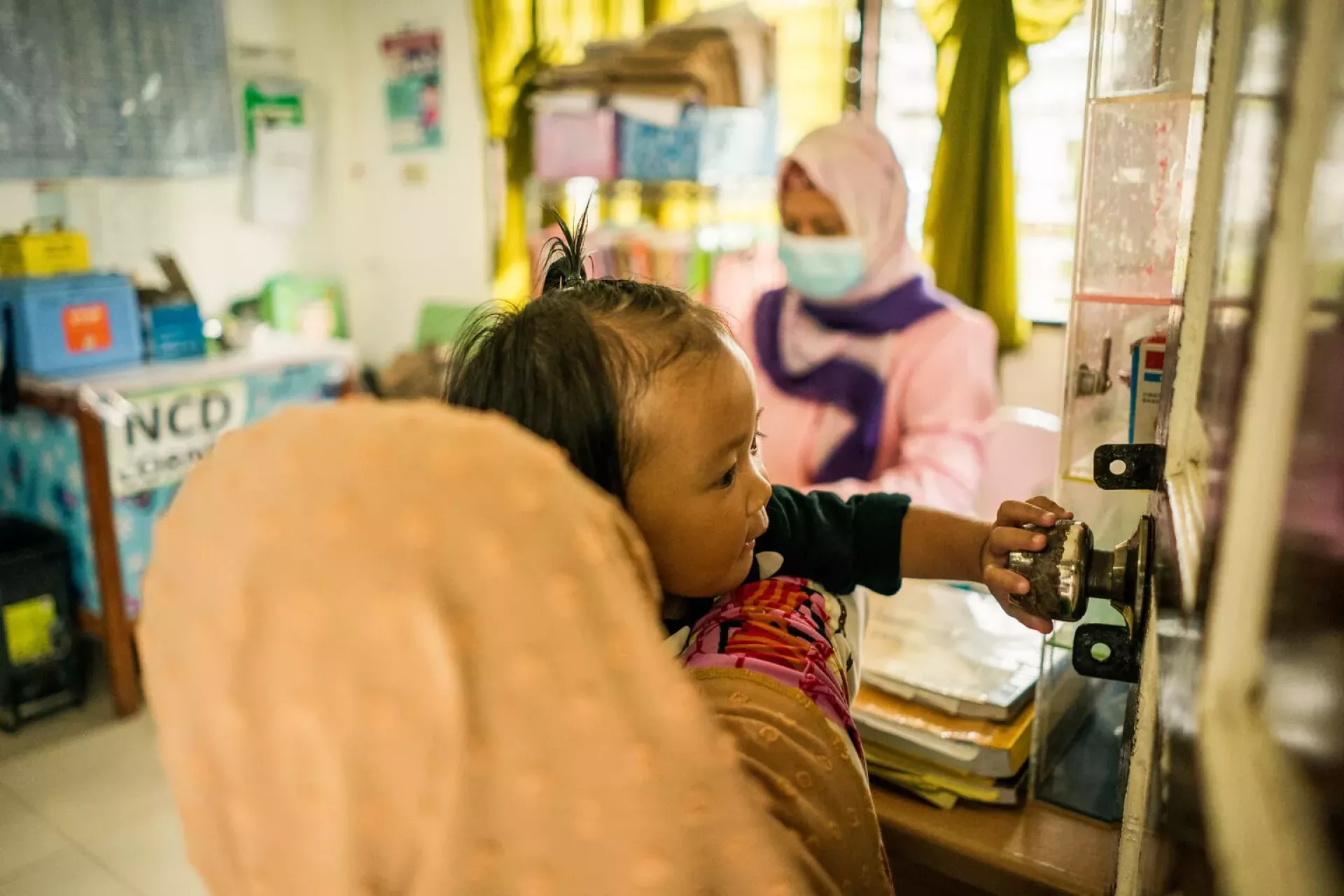 In Marantao, BARMM, Philippines, Jamila (beige hijab) holds her 13-month-old daughter Jonaila while during a routine medical checkup at a rural health center.
