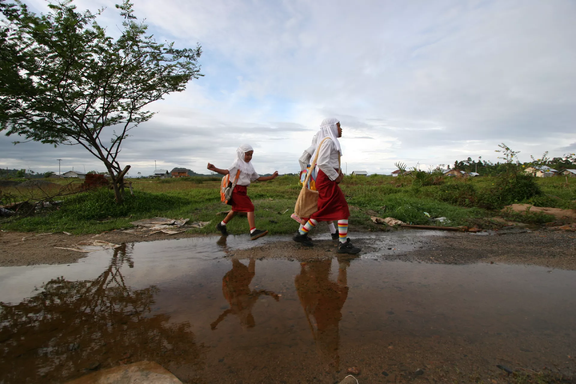 Girls walk to their new school together, avoiding a large puddle, near Calang, Indonesia